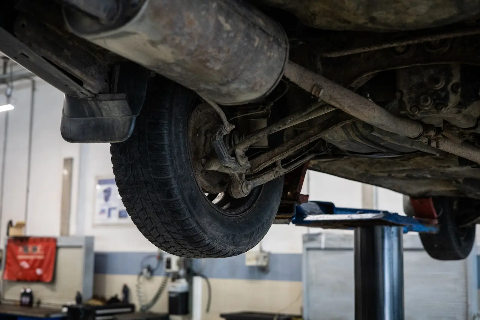 Car raised on a shop lift showing the tire, suspension and exhaust from underneath